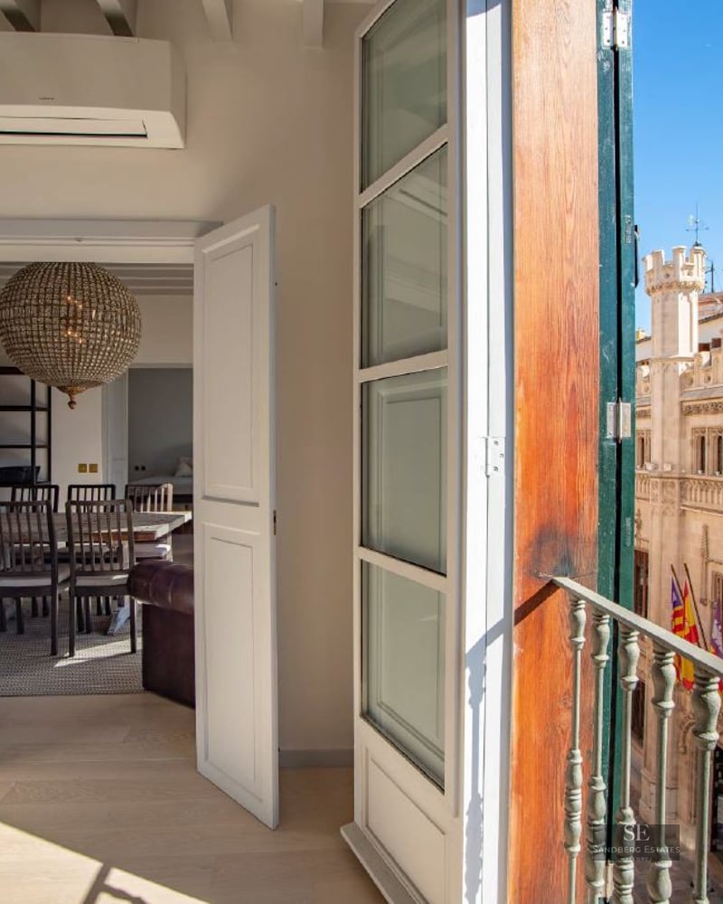 View from an open balcony door looking out at a historic Gothic stone building under a clear blue sky.