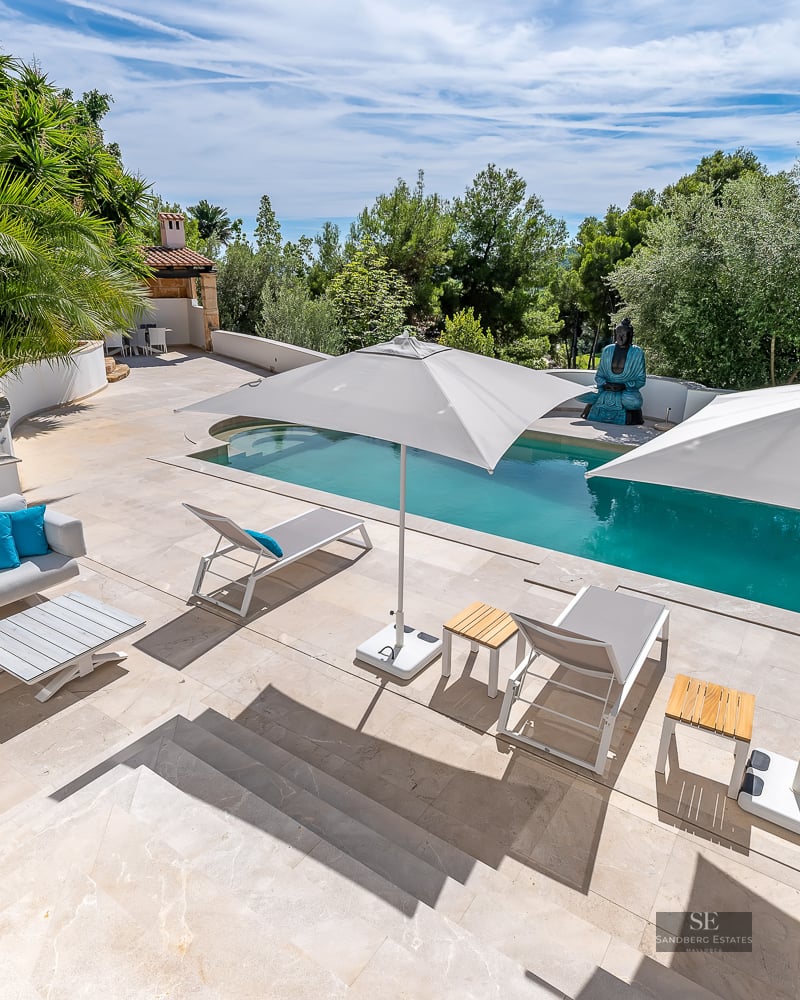 A sun-drenched outdoor pool area with white sun loungers, umbrellas, and a lounge sofa with turquoise cushions.