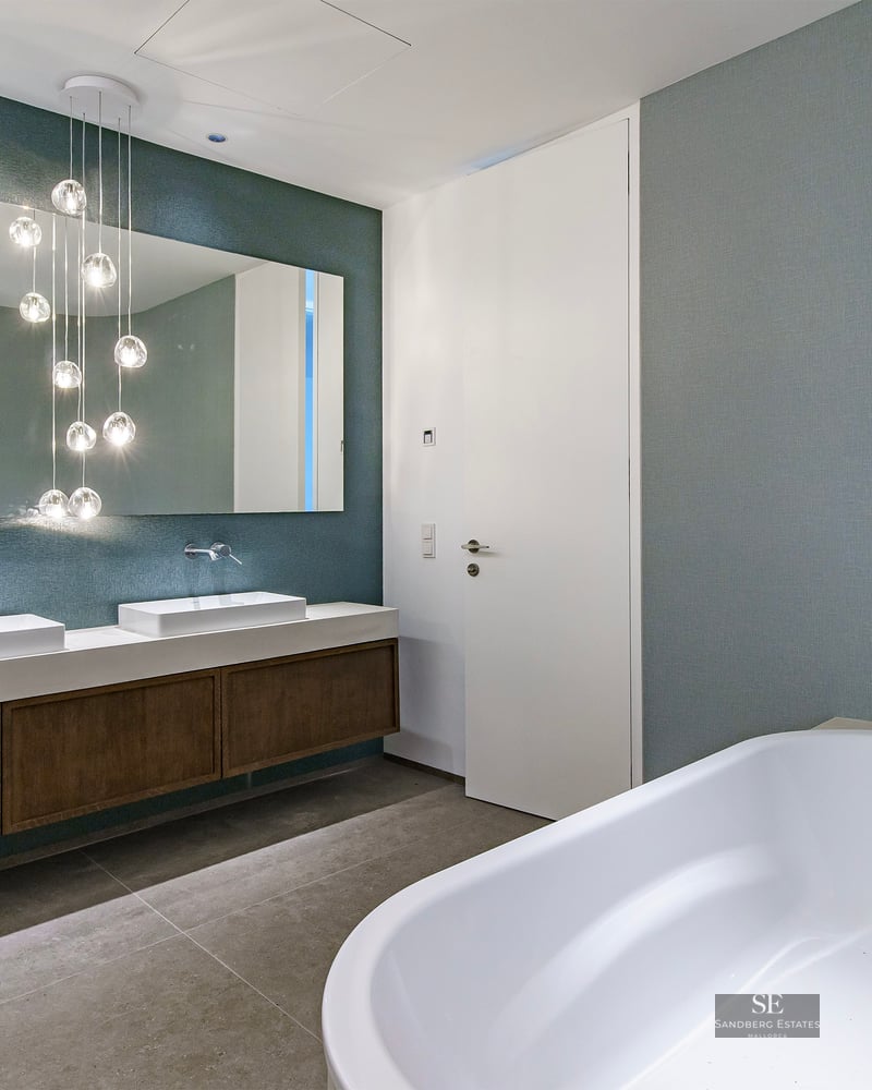 Luxury bathroom featuring a white bathtub, double vanity with wooden cabinets, and hanging glass globe lights.