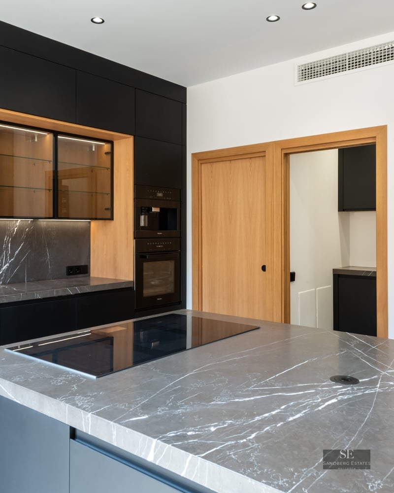 Modern kitchen featuring matte black cabinets, grey marble countertops, and warm wood accents.