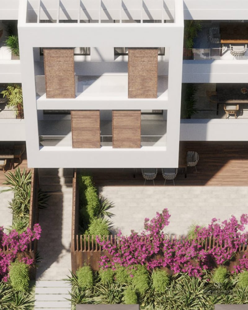 Bird's eye view of a white modern building with spacious terraces, wooden shutters, and lush flowering gardens.