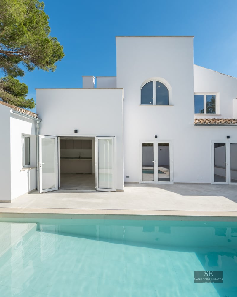 Turquoise swimming pool in front of a clean white modern Mediterranean villa under a clear blue sky.