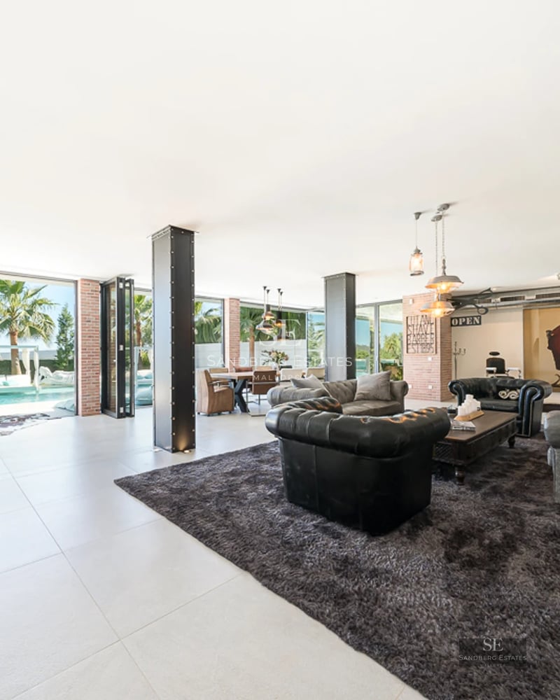 Aerial view of modern villa featuring a bright blue pool, lush garden, and minimalist architecture. Expansive terraces and abundant natural light.