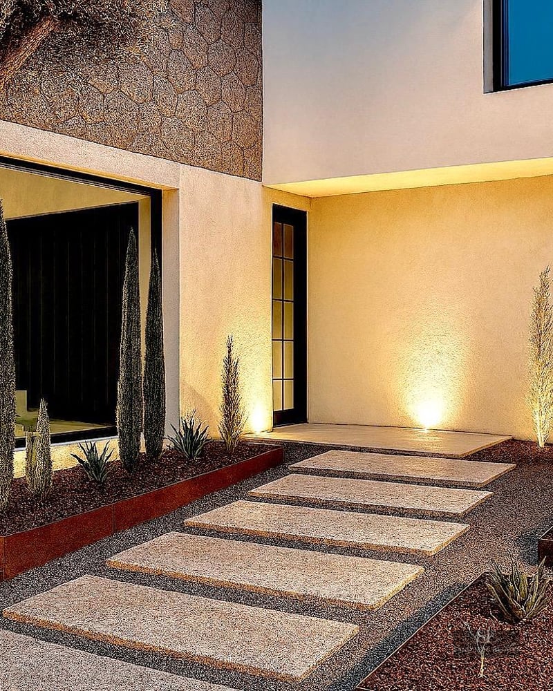 Modern house entrance at night with a stone step path, an olive tree, and integrated lighting.
