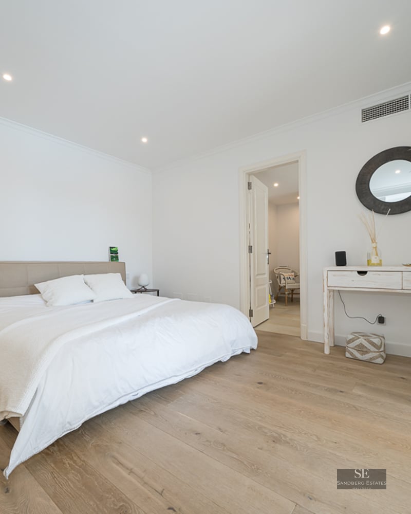 Chambre principale lumineuse avec lit blanc, parquet clair et console minimaliste avec miroir rond.
