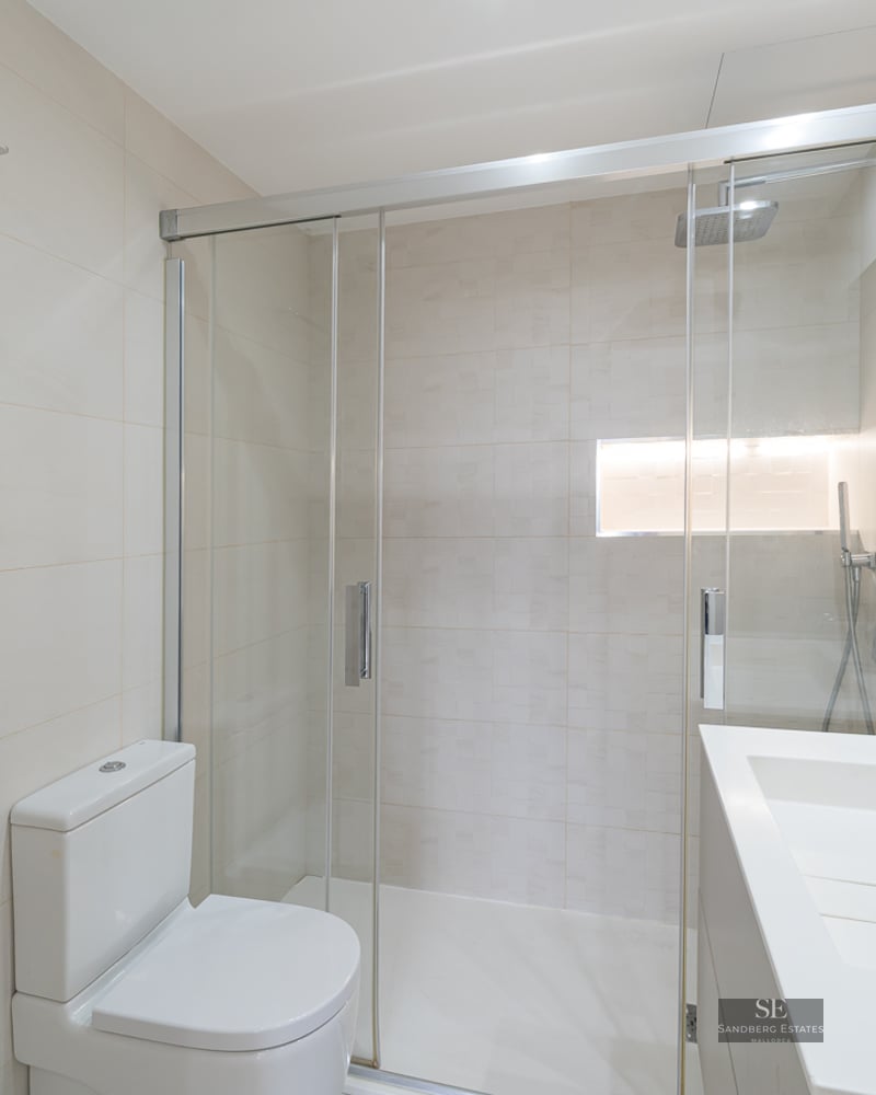 Bright modern bathroom with a glass walk-in shower, white toilet, and minimalist sink vanity.