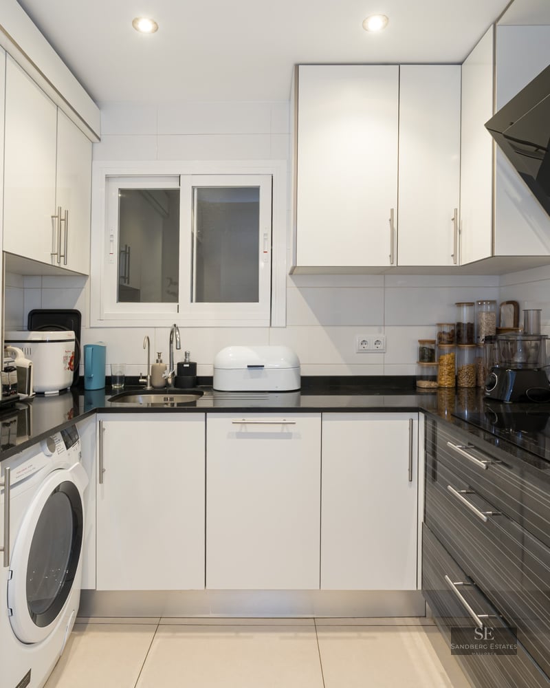 Cuisine moderne en U avec placards blancs, plans de travail noirs et appareils en acier inoxydable.