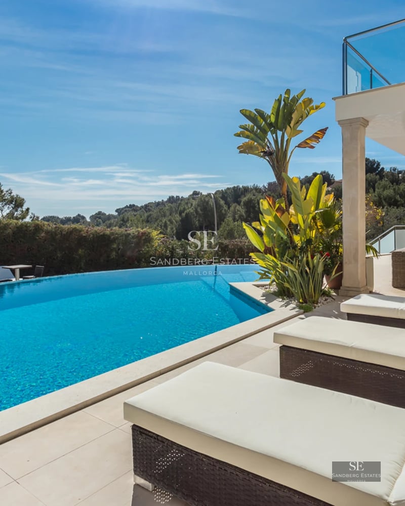 Exterior view of modern villa with infinity pool, lush garden, and minimalist architecture. White facade with large windows and natural light.