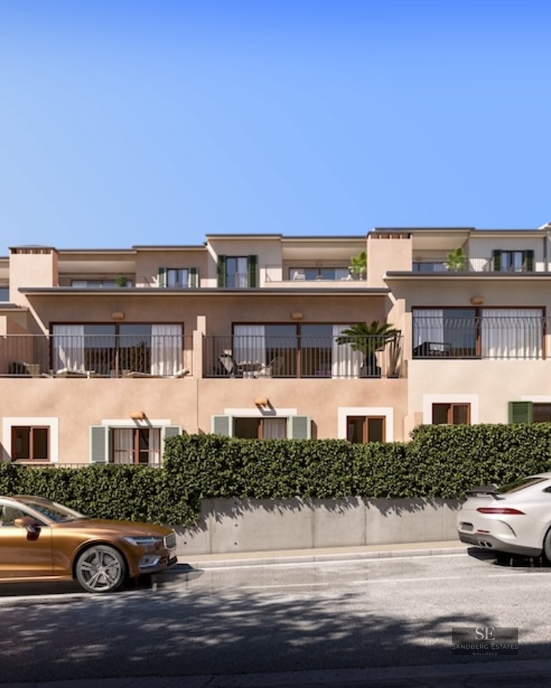 Modern apartment building with balconies, stone walls, and luxury cars parked on the street under a clear blue sky.