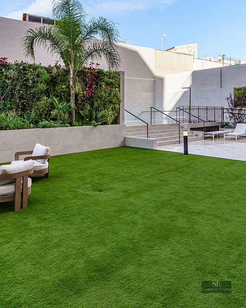 Modern outdoor lounge area with white sofas on a green lawn next to a vertical garden and a pool deck with sun loungers.
