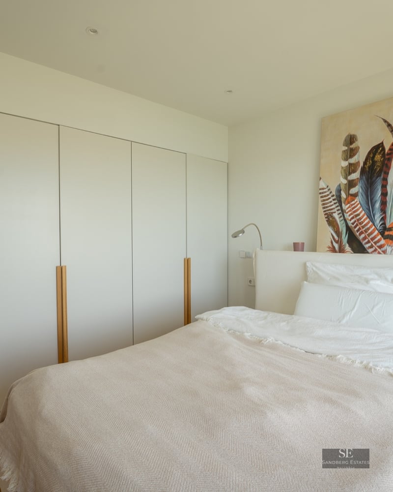 A bright bedroom featuring a white bed, large floor-to-ceiling built-in wardrobes, and feather artwork.