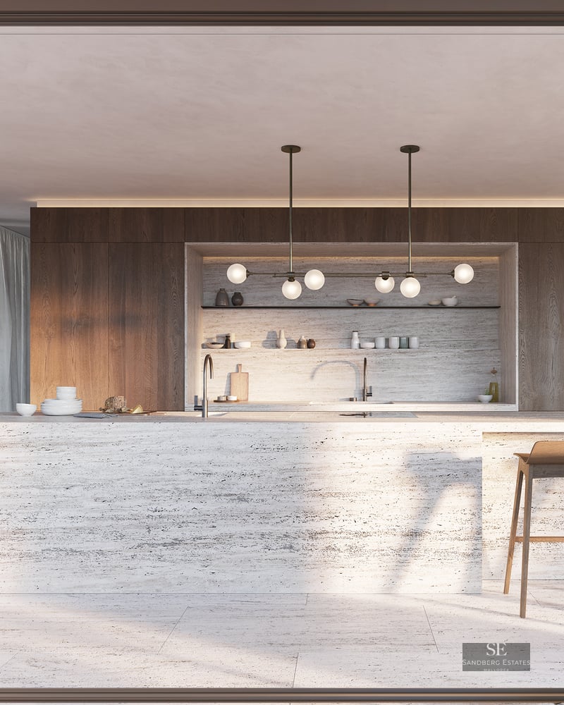 A large travertine kitchen island with wooden stools in a modern open-plan space with floor-to-ceiling windows.