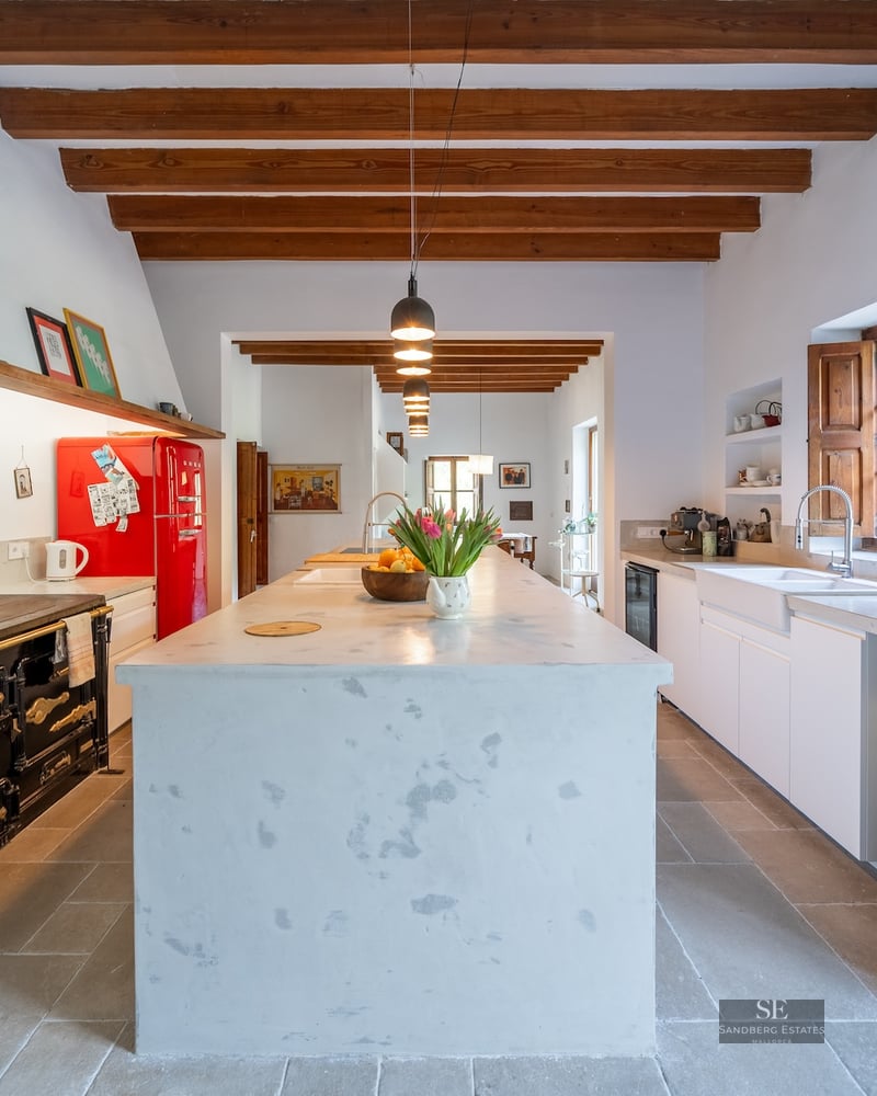 Spacious kitchen featuring a large white central island, exposed wooden beams, a retro red fridge, and a cast-iron stove.