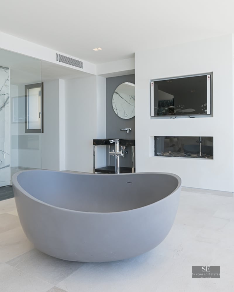Modern bathroom featuring a grey freestanding tub, marble-walled shower, and dual vanities with round mirrors.
