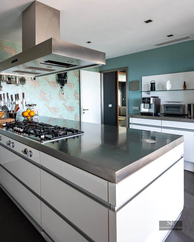 A luxury kitchen featuring a central stainless steel island, fish-patterned wallpaper, and high-end appliances.