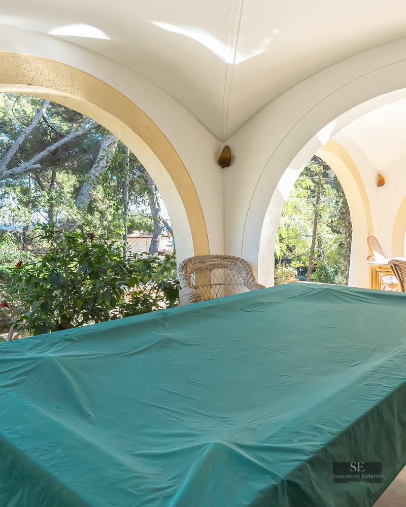 Large covered terrace with white arches, a pool table covered in green cloth, and garden views.