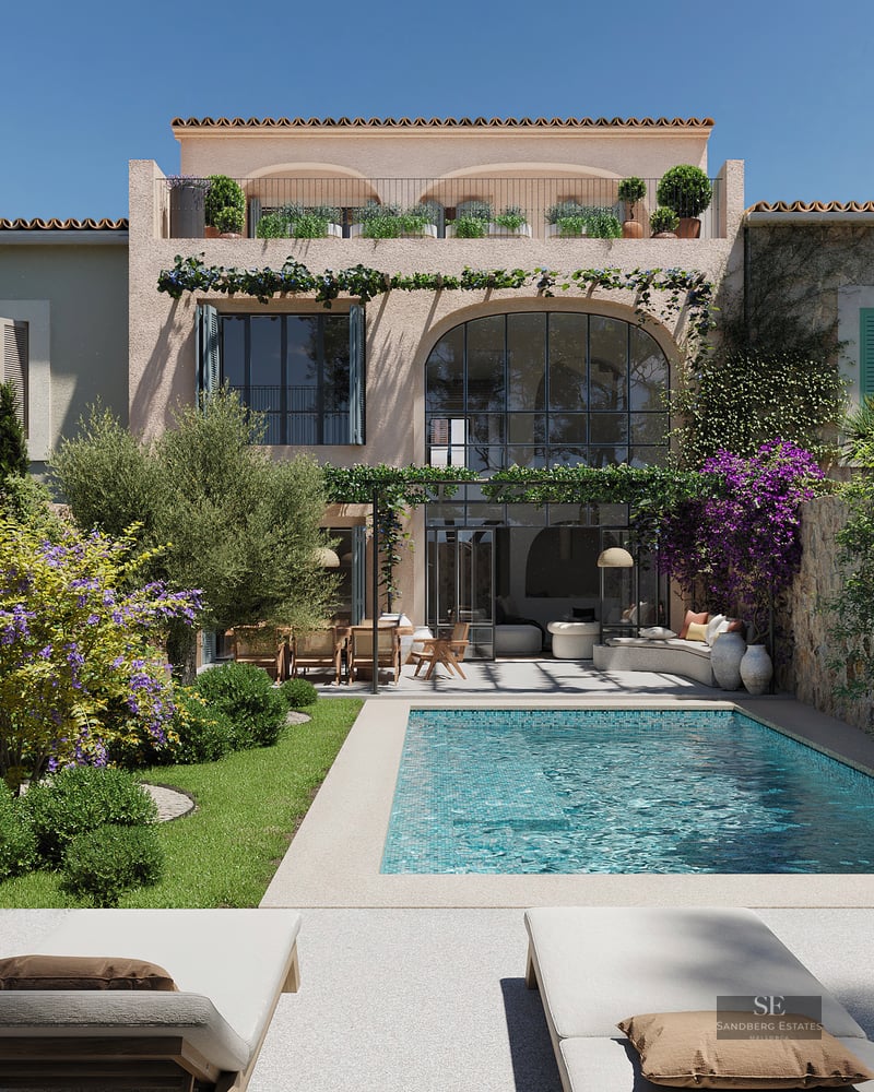 Turquoise swimming pool surrounded by a lush garden and Mediterranean villa facade under a clear blue sky.