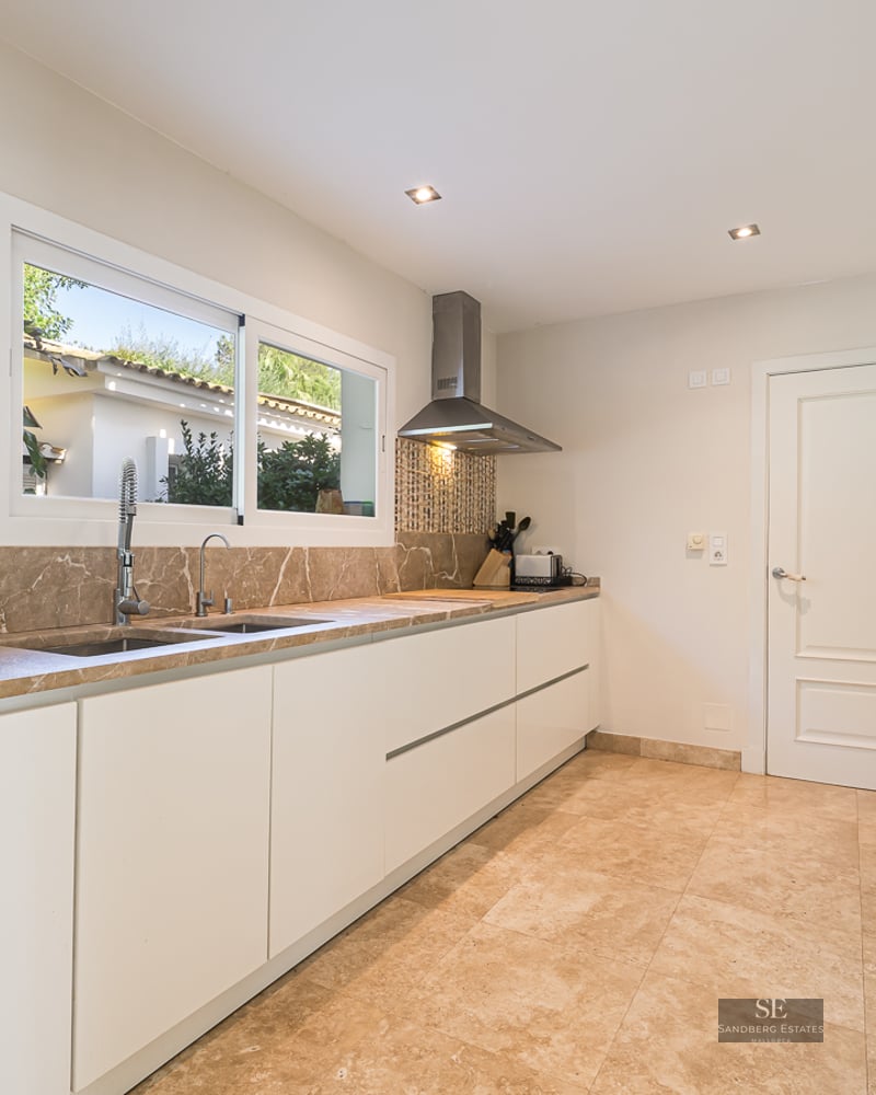 Modern kitchen with white cabinets, marble counters, stainless steel appliances, and a window viewing the outdoors.