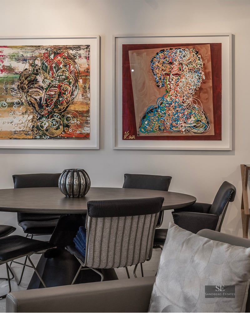 Modern dining room featuring a dark round table, designer chairs, and two large abstract paintings on a white wall.