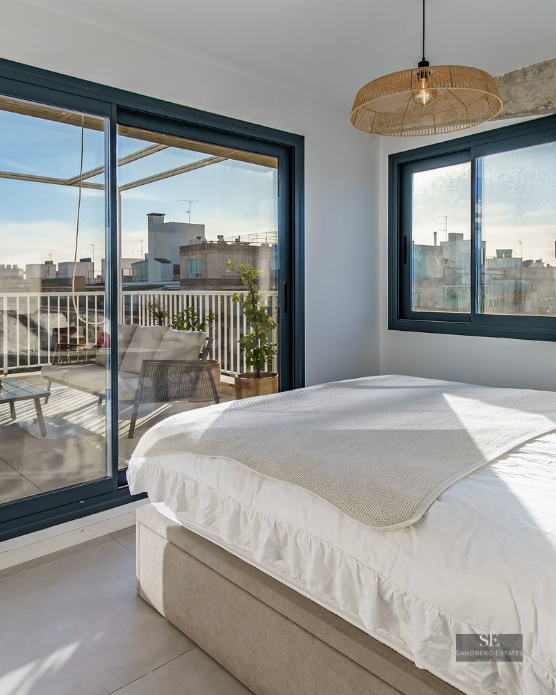 Bright bedroom with white bedding and large sliding glass doors opening to a private terrace with city views.