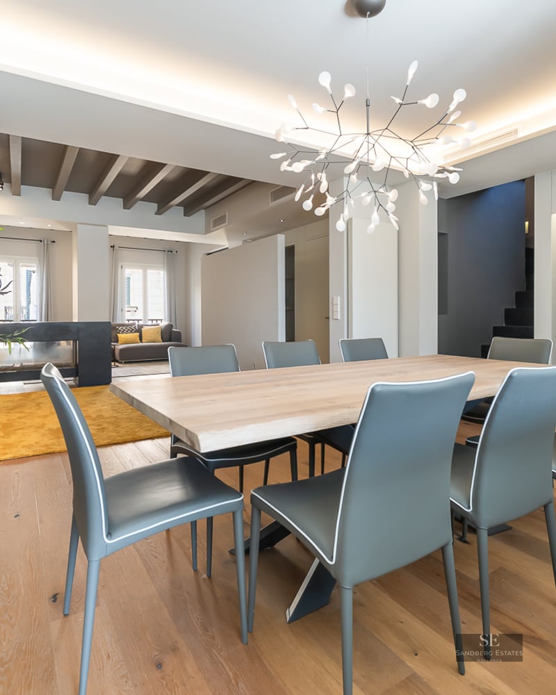 Spacious modern dining room featuring a large wooden table, grey chairs, and a branch-style designer chandelier.