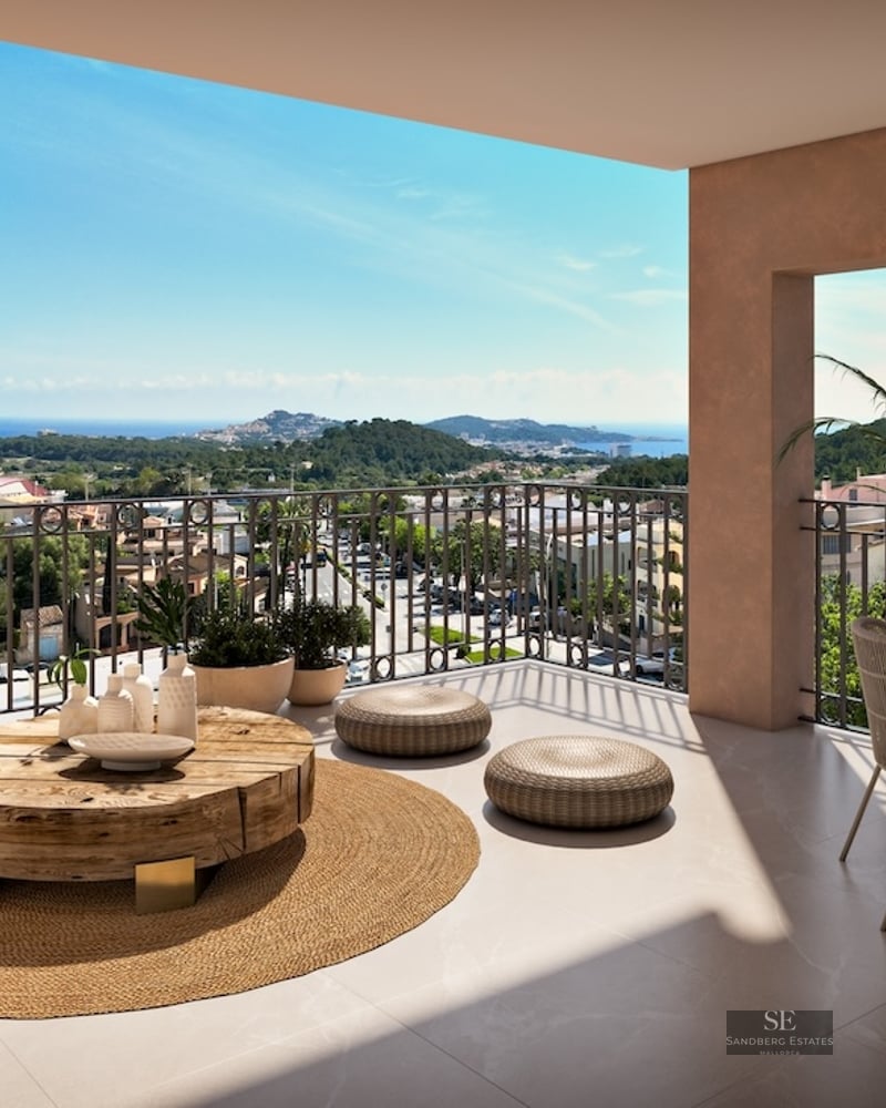 Spacious modern terrace with organic wood furniture and a jute rug overlooking a Mediterranean coastal town and sea.