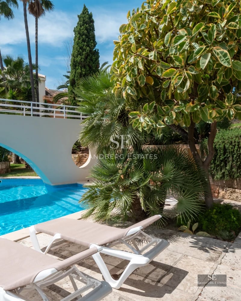 Exterior view of a modern villa with infinity pool, lush garden and minimalist architecture. Natural stone facade and large glass windows.