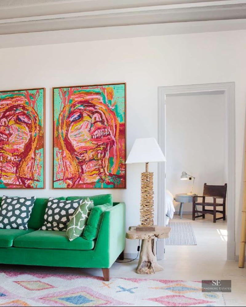 Bright living room featuring a green velvet sofa, two large colorful portraits, and high beamed ceilings.