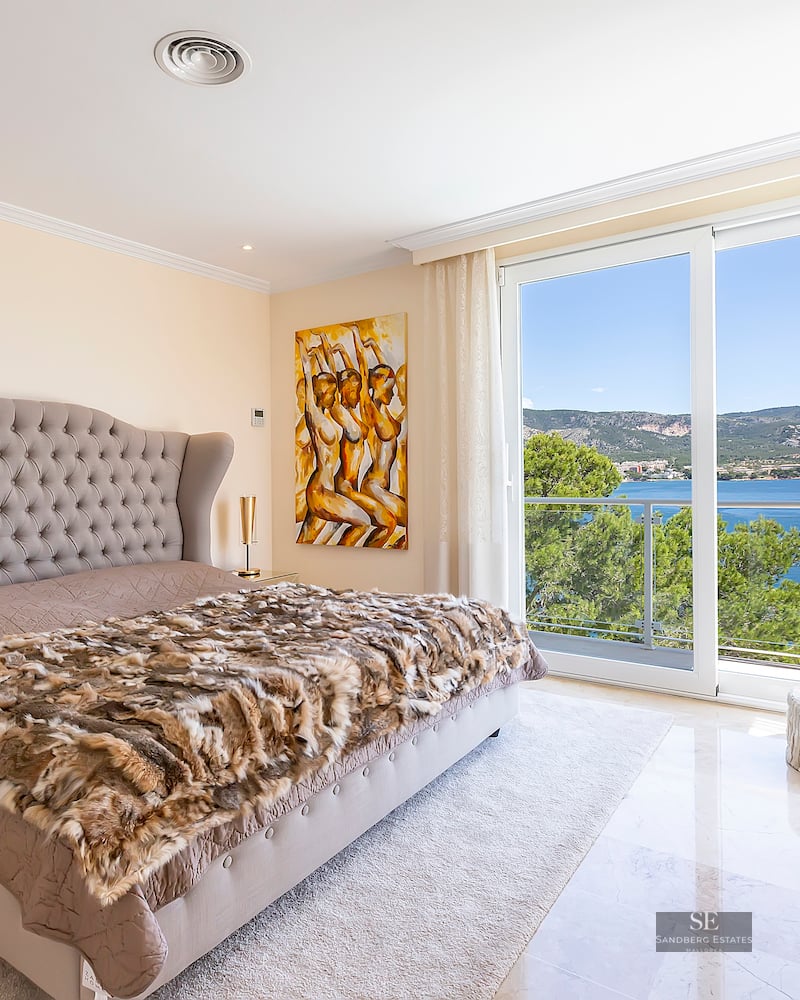 Luxurious bedroom featuring a large tufted bed, marble floors, and sliding glass doors revealing a panoramic sea view.