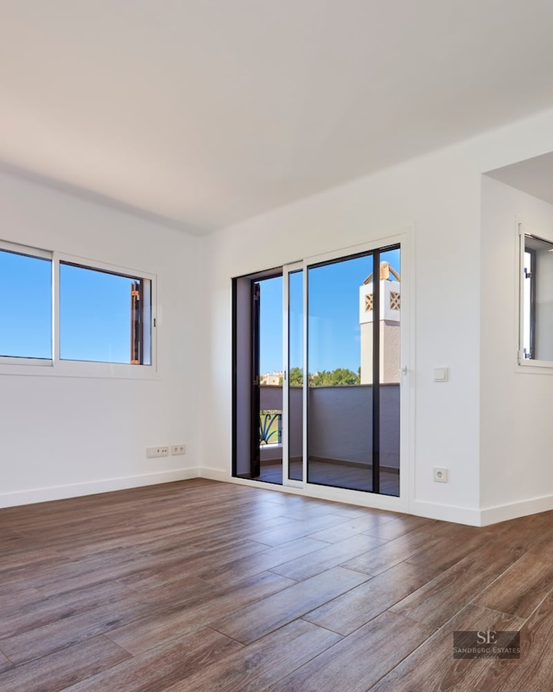 Empty room with white walls, wood-effect tile floors, and a sliding glass door leading to a terrace.