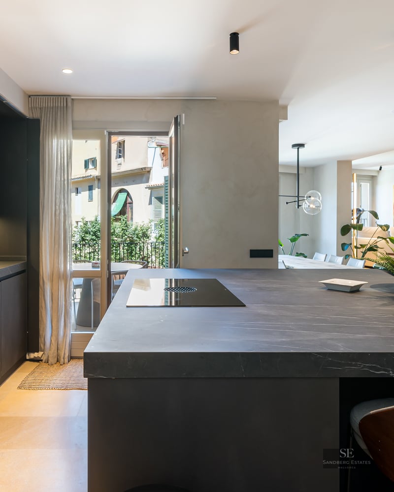 Modern dark stone kitchen island in an open-concept apartment with living area in the background.