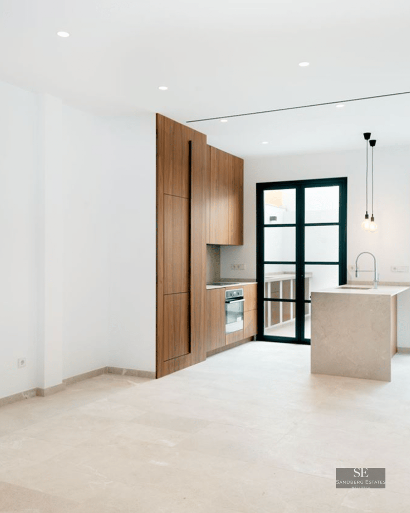 Modern kitchen with wood cabinets, stone island, and large black-framed glass doors leading to a terrace.