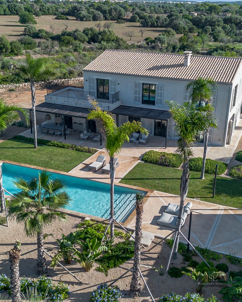 Aerial view of a luxury villa with a turquoise swimming pool, palm trees, and landscaped gardens.