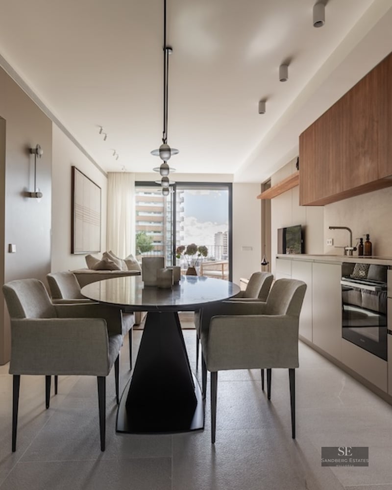 Contemporary dining room featuring a black oval table, grey upholstered armchairs, and a sleek minimalist kitchen.