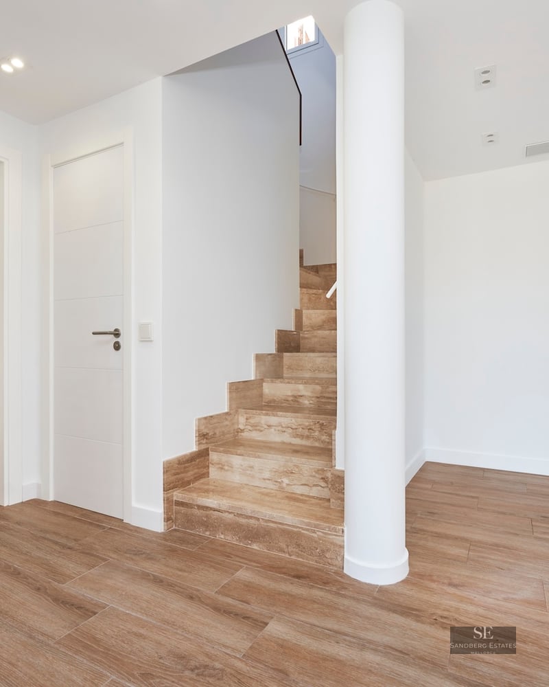 Modern hallway featuring a light stone staircase, white walls, wood-look porcelain floors, and a white structural column.