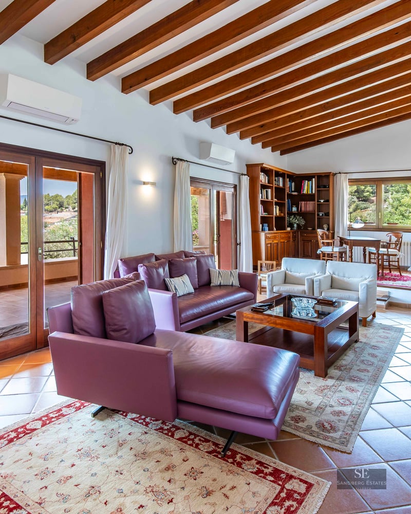 Bright living room with purple leather sofas, wooden ceiling beams, terracotta tiles, and terrace views.