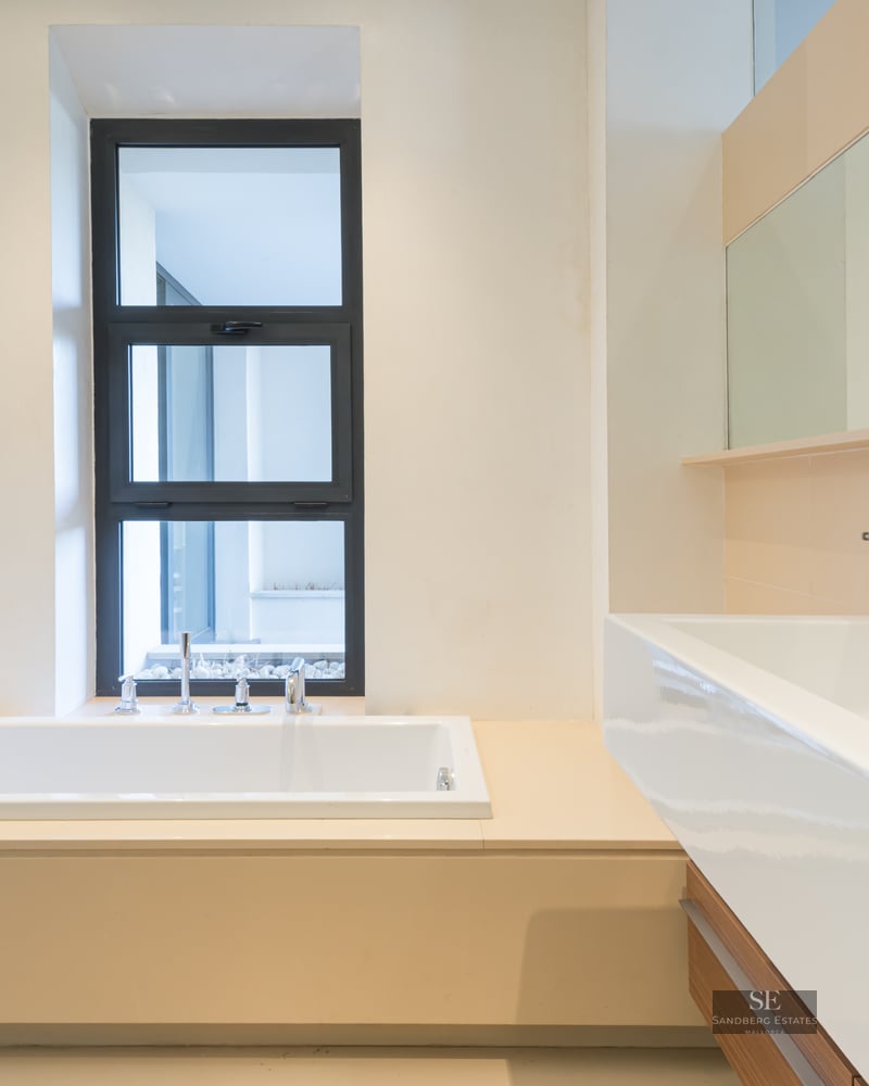 Modern bathroom featuring a built-in white bathtub next to a window and a large white rectangular sink with a wide mirror.