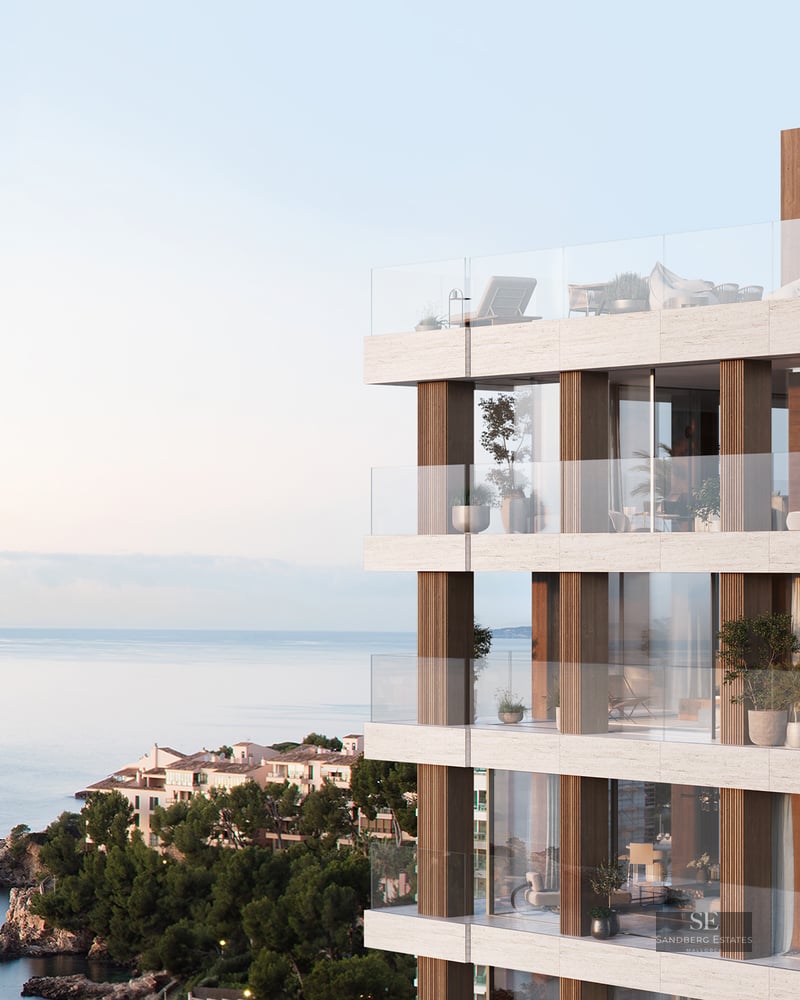 Modern multi-story building with stone facade, glass balconies, and panoramic sea views at sunset.