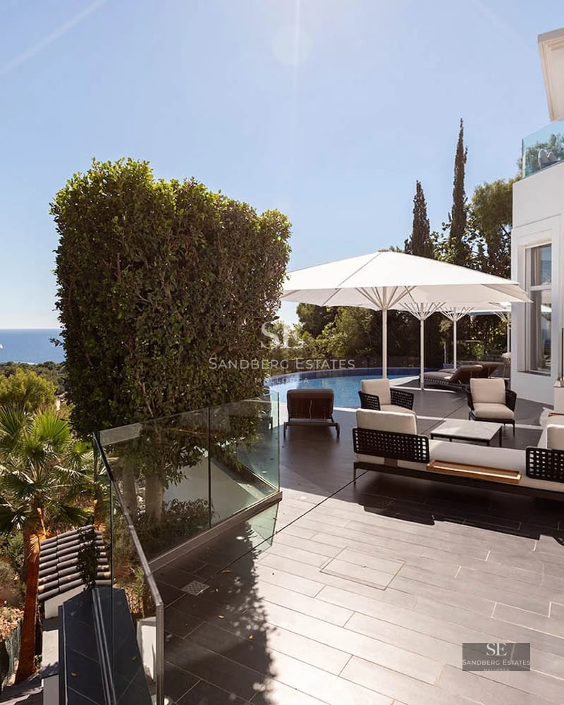 Spacious modern white villa terrace with designer outdoor furniture, an infinity pool, and panoramic ocean views.