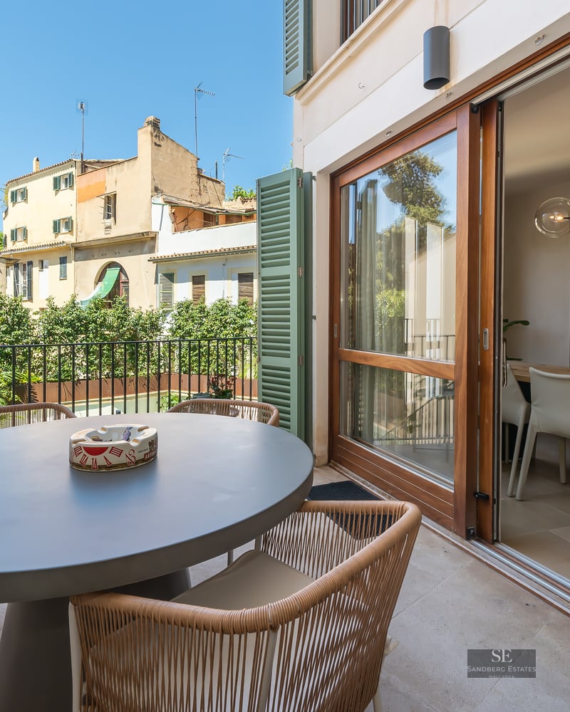 Sunny terrace with a gray oval dining table and wicker chairs next to large sliding glass doors.