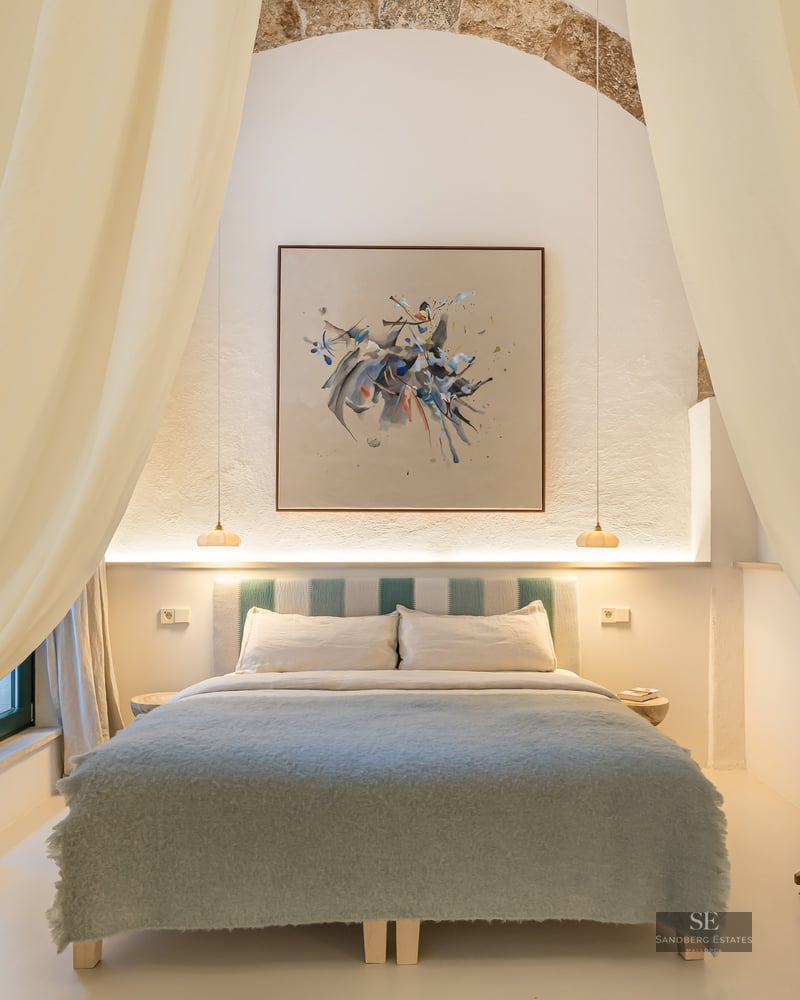 Chambre élégante avec arche en pierre, art abstrait et literie bleu doux encadrée par de grands rideaux crème.