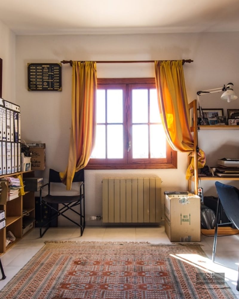 A home office with a wooden desk, telescope, bookshelves, yellow curtains, and certificates on the walls.