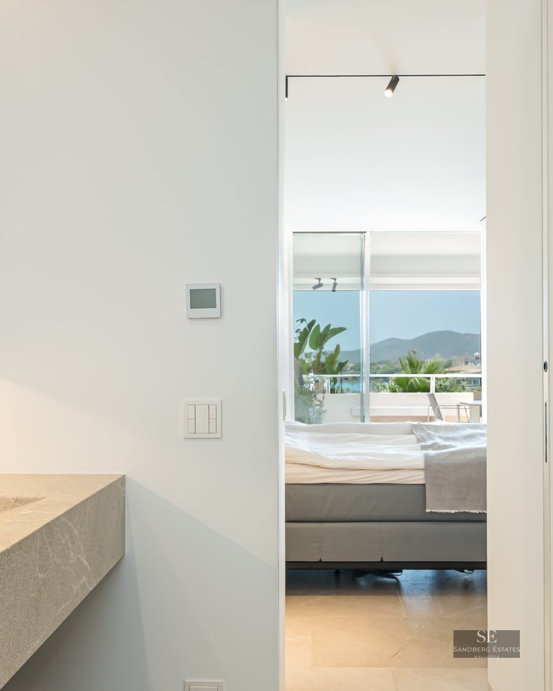 Modern bathroom with a stone sink and black faucet, looking through a doorway into a bedroom with a mountain view.