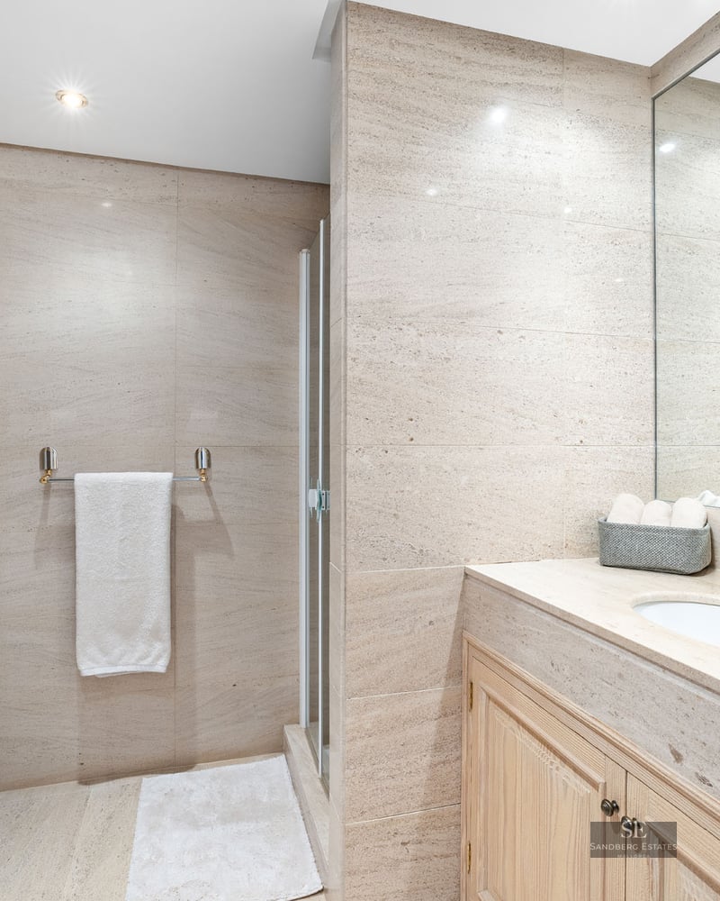 Salle de bain moderne avec murs en pierre beige, bidet blanc, meuble en bois avec lavabo et grand miroir.