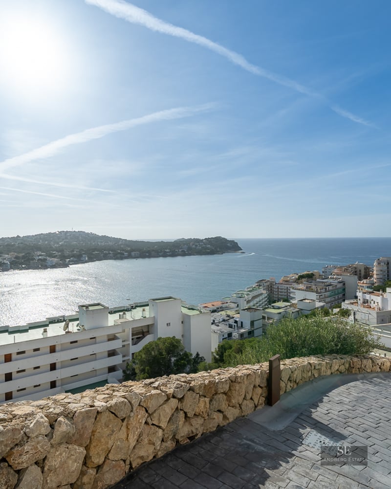 Elevated view of a blue Mediterranean bay with white coastal buildings under a bright sunny sky.