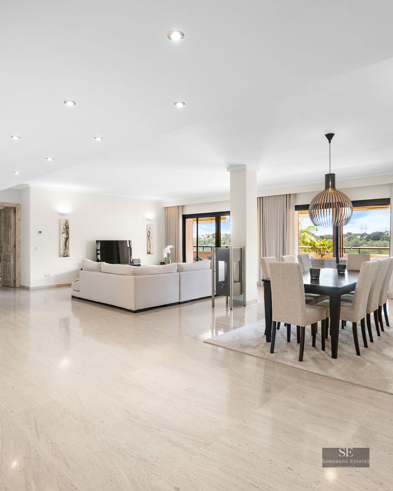 Intérieur lumineux à aire ouverte avec sols en marbre poli, un grand canapé blanc et une salle à manger moderne.