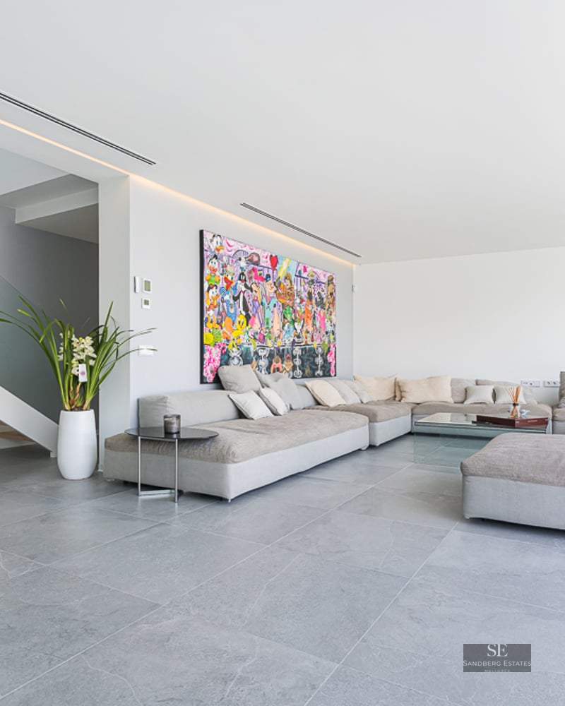Spacious living room with large grey modular sofa, colorful wall art, and glass-railing staircase.
