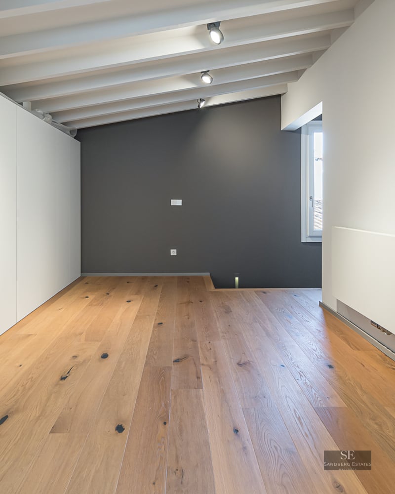 Empty bedroom featuring light wood floors, a white beamed ceiling, gray accent wall, and large white wardrobes.