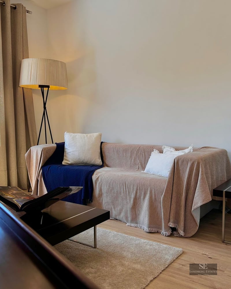 Beige sofa with blue throw, floor lamp, and purple orchid in a bright living room with wooden floors.