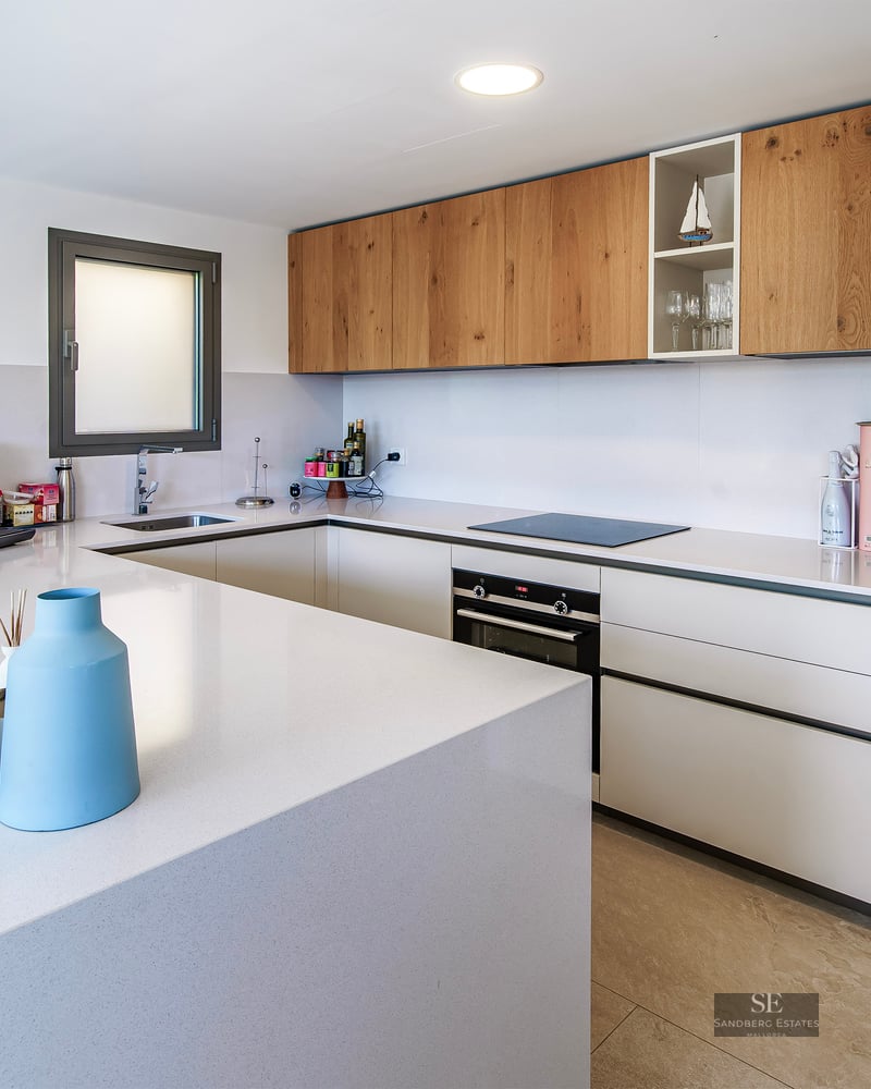 Modern white kitchen with wooden upper cabinets, a large white island, and built-in appliances.
